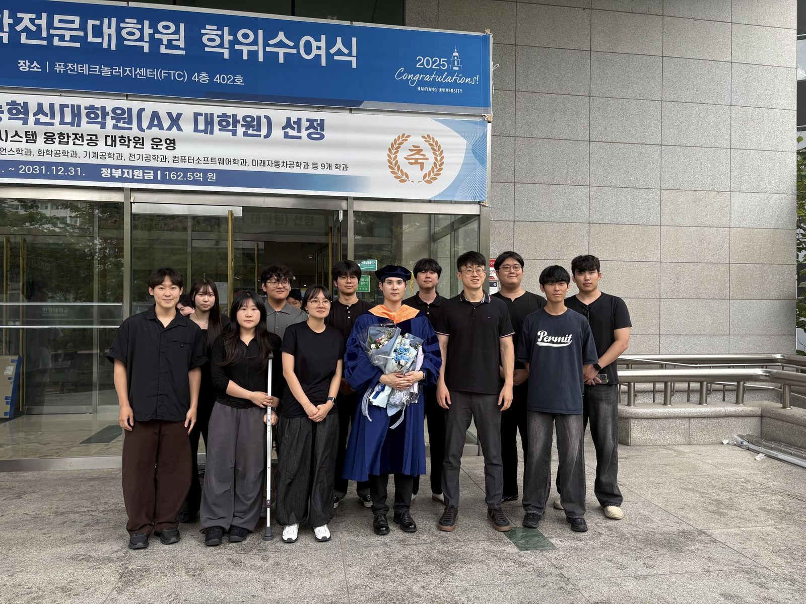 Dr. Tae Hyung Kim in doctoral regalia with the full lab group at the August 2026 graduation ceremony